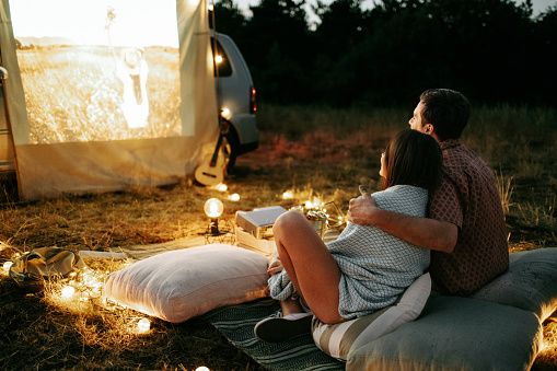Junges Paar sitzt bei einer Autokino-Veranstaltung vor einem Auto und vermittelt eine ernsthafte Begegnung, Kommunikation und die ersten Momente einer dauerhaften Beziehung.
