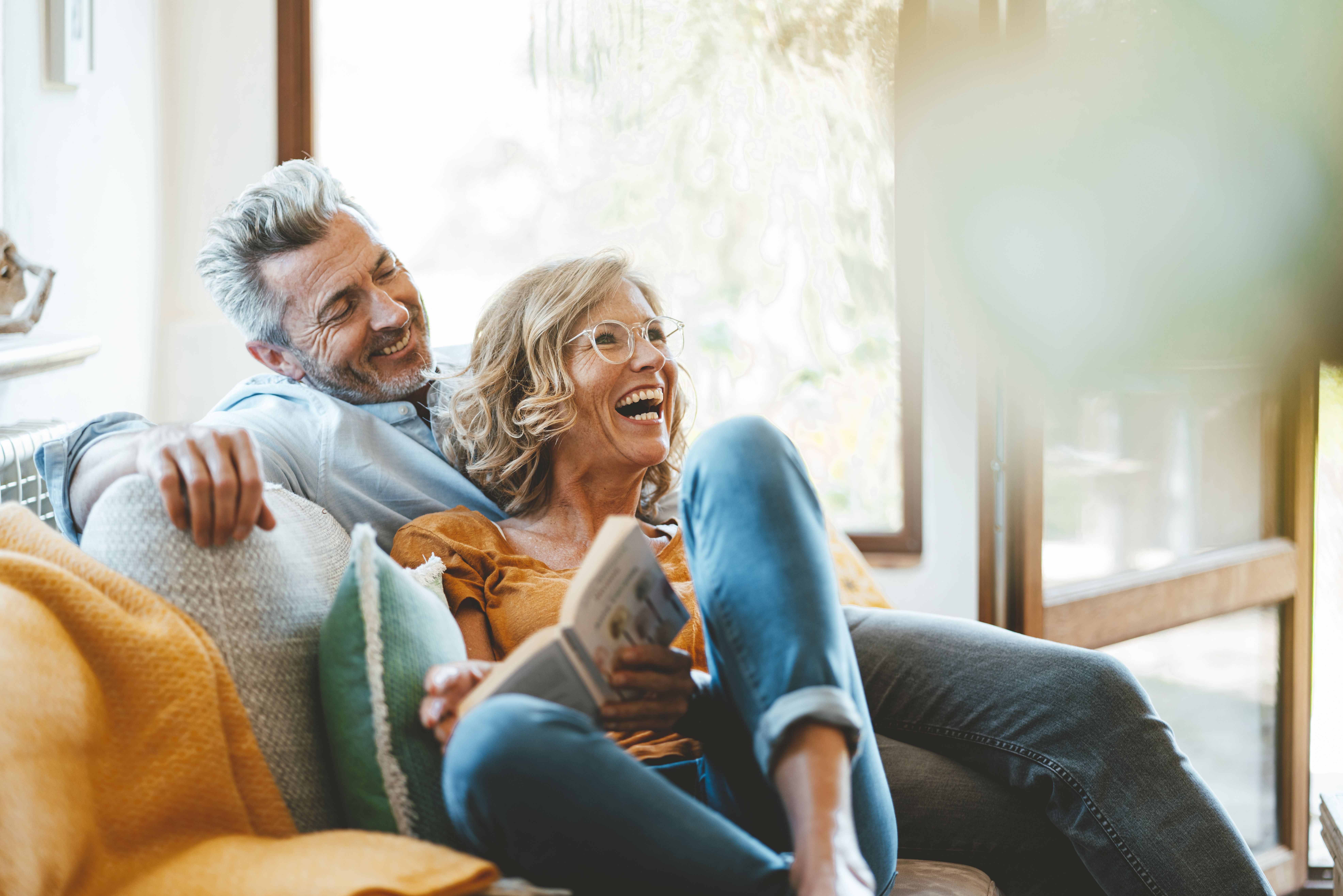 Lächelndes Paar um die vierzig auf einem Sofa zu Hause, das einen Moment der Verbundenheit teilt und eine dauerhafte Beziehung, gemeinsame Werte und eine gelungene ernsthafte Begegnung vermittelt.