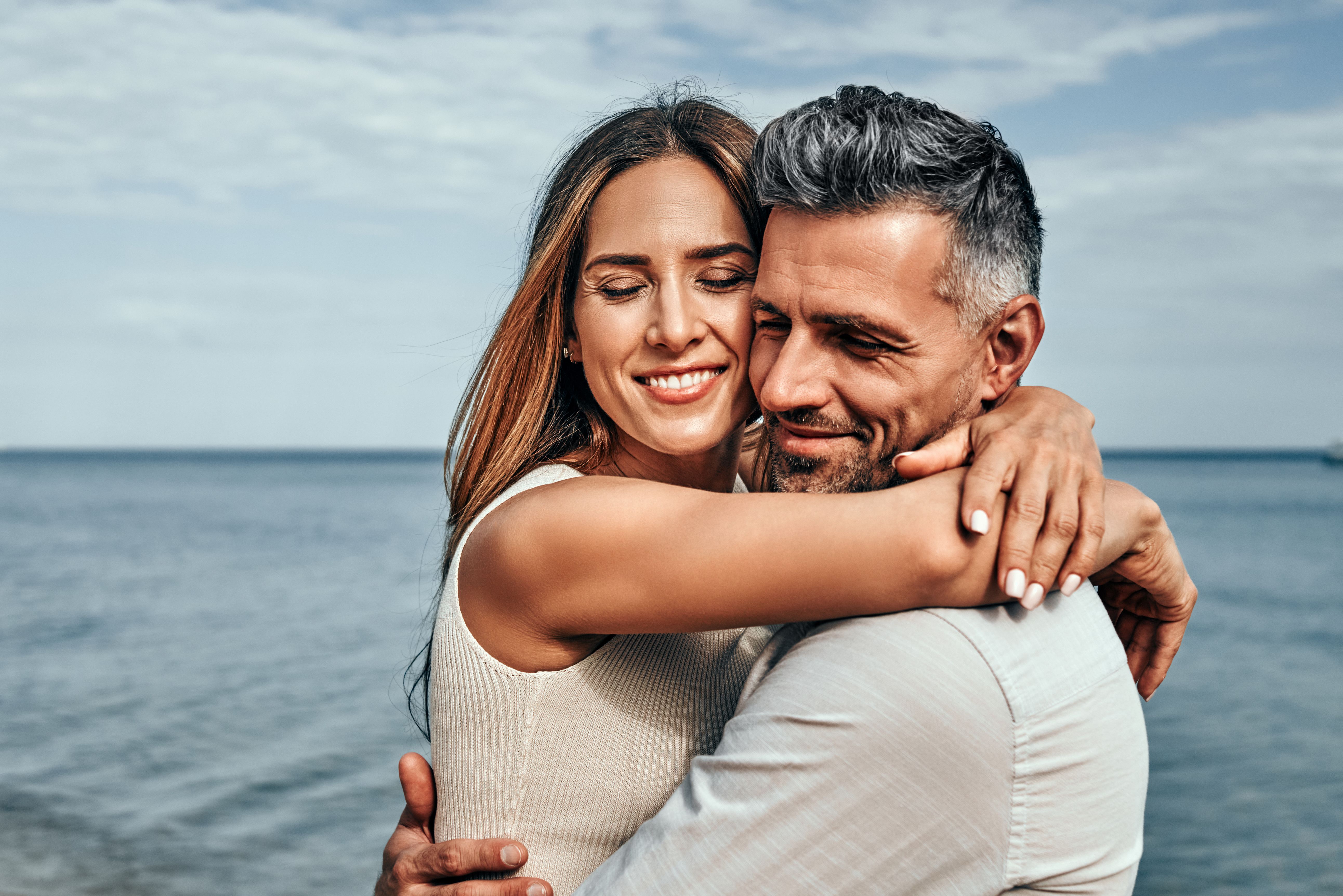 Paar in den Vierzigern, das sich am Strand im Sommer umarmt und eine ernsthafte Begegnung, eine dauerhafte Beziehung und Vertrauen zwischen Partnern veranschaulicht.