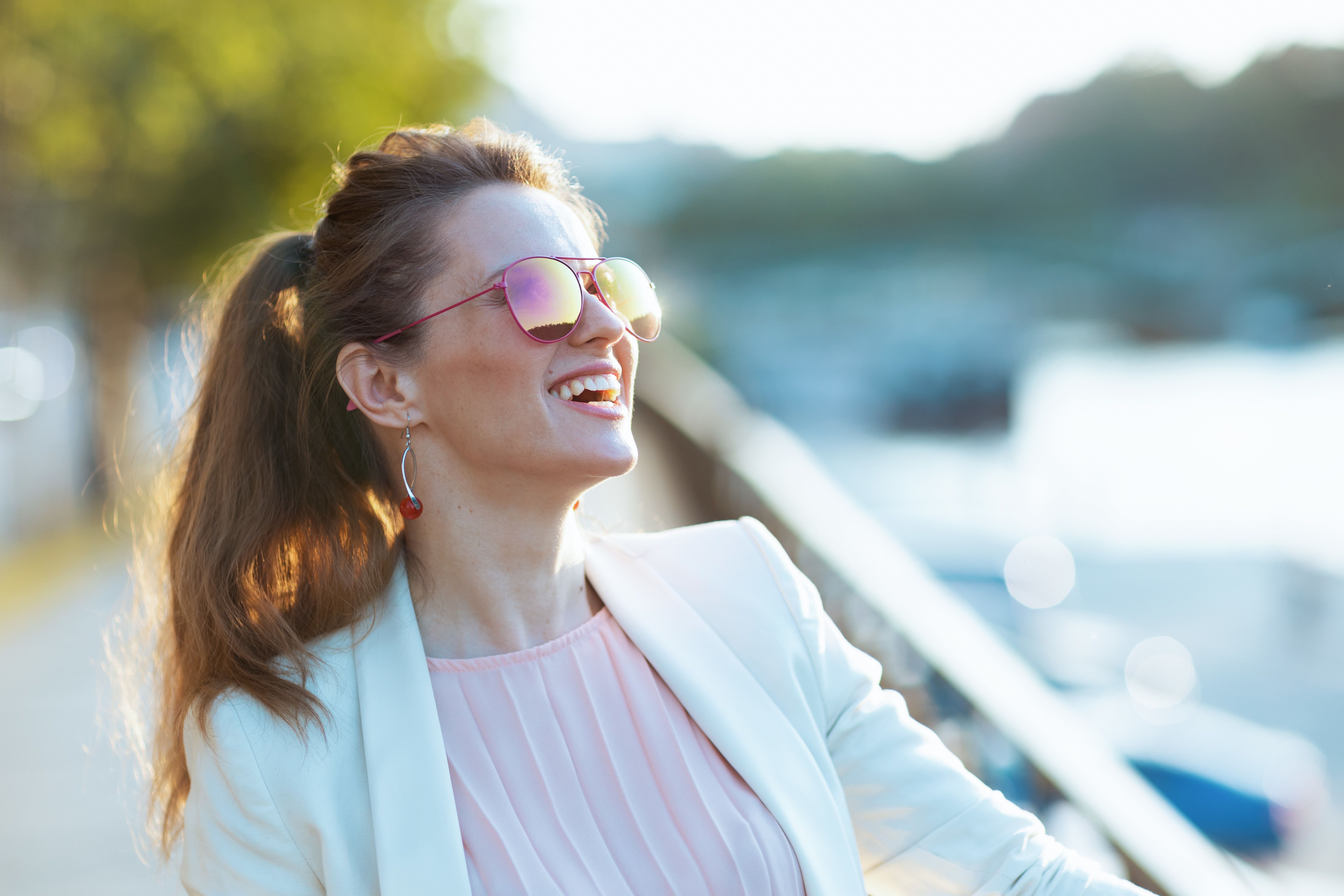 Lächelnde junge Frau mit Sonnenbrille, die auf einer Terrasse sitzt und auf ihr erstes Date nach einer Begegnung auf einer seriösen Partnerbörse wartet.