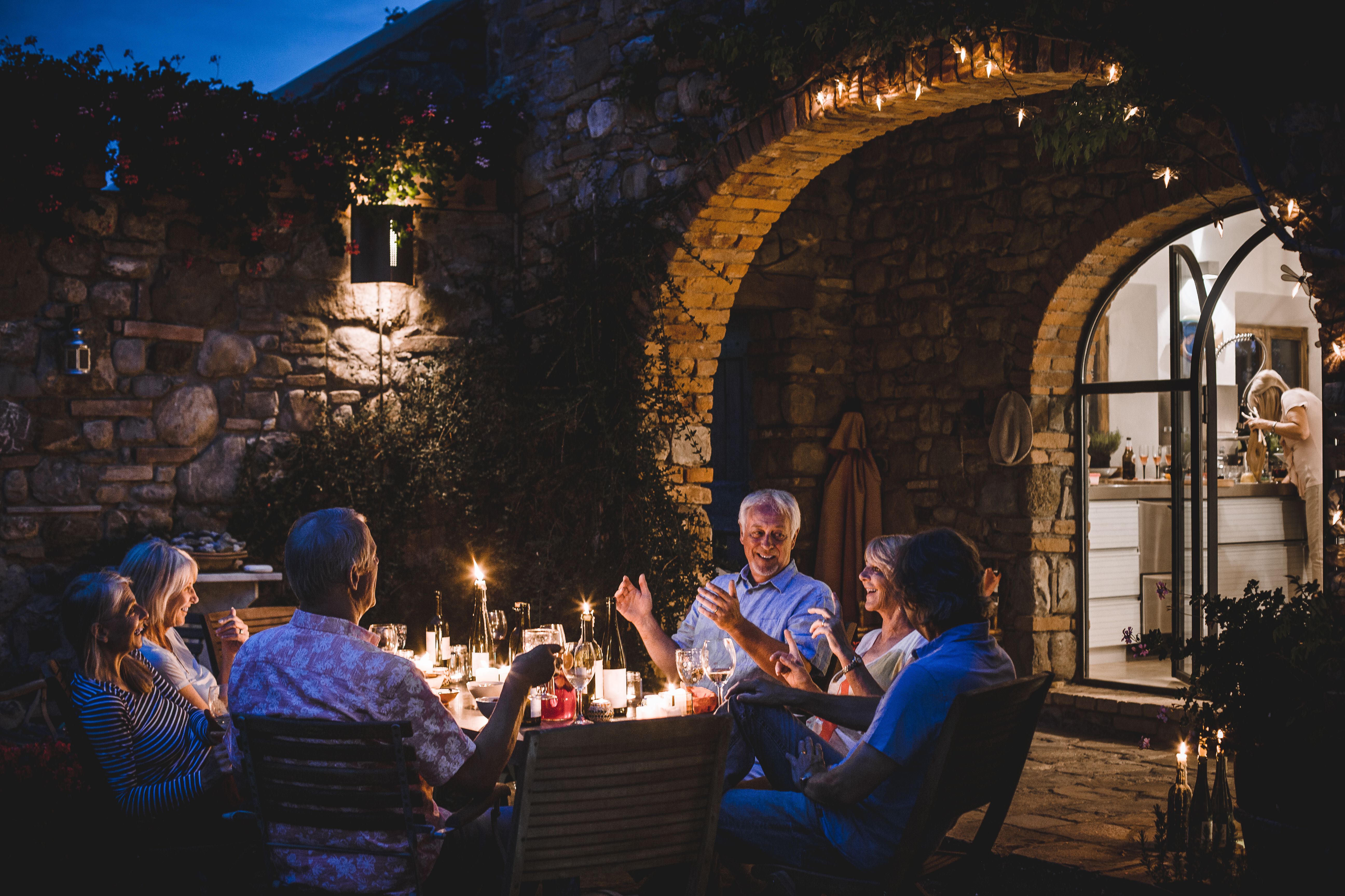Gruppe lächelnder Freunde beim Abendessen im Garten, als Bild für einen Neuanfang, authentische Begegnungen und ein wieder aufblühendes Sozialleben nach einer Scheidung.