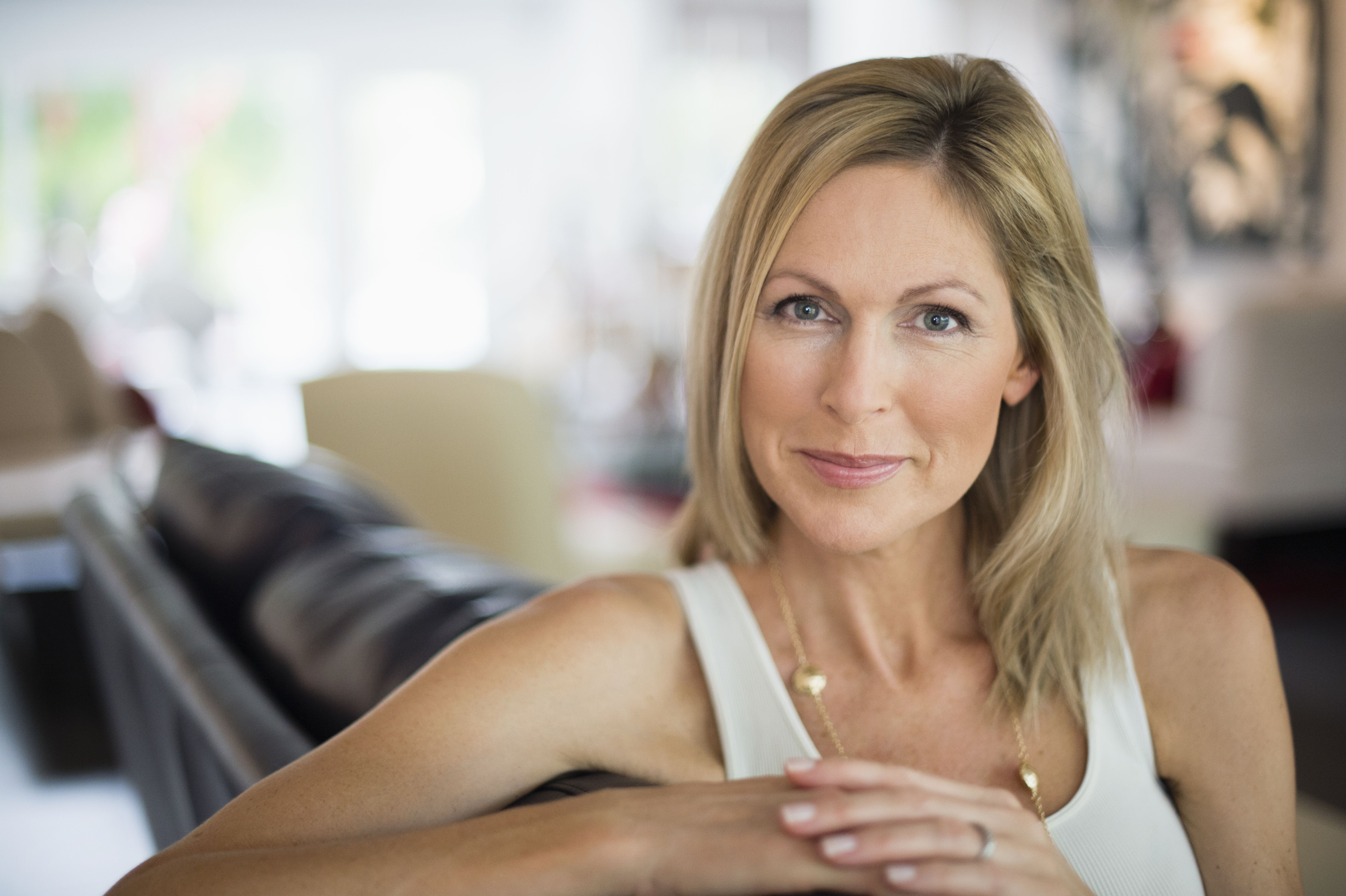 Frau über 40, die in ihrem Wohnzimmer sitzt und selbstbewusst in die Kamera blickt, als Bild für einen Neuanfang und die Suche nach einer ernsthaften Beziehung nach einer Scheidung.