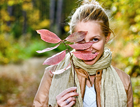 Attraktive blone Frau schaut durch ein Herbstblatt und lächelt