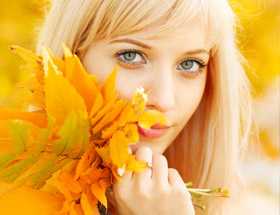 Attraktive blone Frau schaut durch ein Herbstblatt und lächelt