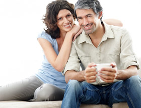 Mann und Frau sitzen auf der Couch und lächeln in die Kamera