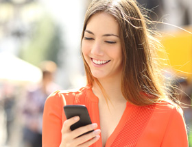 Partnersuche Dornbirn: eine brunette Frau schaut lächelnd auf ihr Smartphone