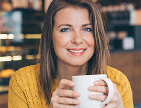 Partnersuche Eisenstadt: Eine brunette Frau im gelben Strickpulover umfasst eine warme Tasse Kaffee